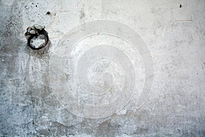 Old white wall covered with dirty plaster with a visible structure. there is a ring on the wall for tying cattle or other animals