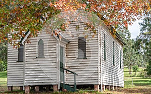 Old white weatherboard rural church surrounded by autumnal trees with multi coloured beautiful leaves