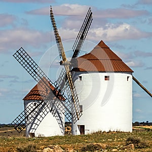 Old white windmills, made of stone, on the field with blue sky and white clouds. La Mancha, Castilla, Spain photo