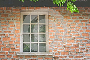 Old white window on brown brick wall on the top of house in vintage style.