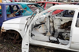 An old white wreck car with open door in a scrap yard that were cleared from interior