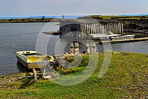 Old white yellow rusty iron boats on green grassy shore of round bay, with wood barn on the water. Lake Baikal