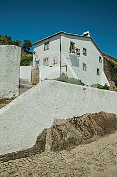 Old whitewashed wall house over rocks with stairs and plants