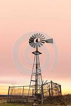 Old wind mill fenced off, with a vibrant moody pink and orange sky