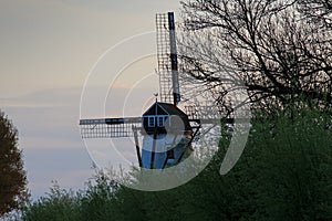 Old windmill with bushes in the late afternoon light and cloudy sky near Bruges