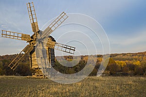 Old windmill in a field near the forest at sunset