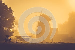 Old windmill at golden sunrise light, misty morning after rain