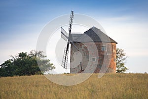 Old windmill on a hill in the rays of the sun at sunset, green fields. Spring rural landscape with an old mill. South Moravia.