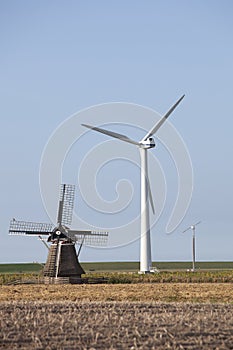 Old windmill and modern turbines together in agricultutre landscape of friesland