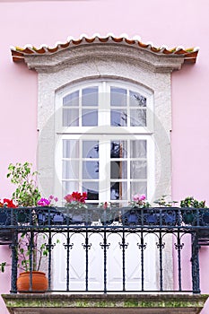 Old window with a balcony on a beautiful pink house facade