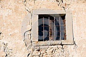 Old window with bars in decayed stone wall