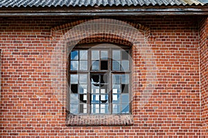 An old window with broken glass panes in a red brick wall