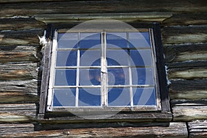 Old window with glass with a blue sky on the background of the wooden wall of the countryside log house