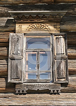 Old window with glass with a blue sky on the background of the wooden wall of the countryside log house