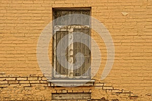 Old window with an iron grill on a brick brown wall