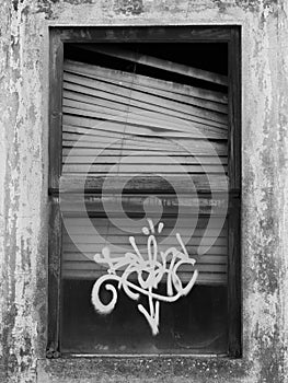 An old window that looks creepy and has a graffity on it on black and white.