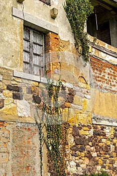 Old window with wooden shutters on a cracked stone and brick wall with ivy