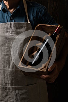 Old winemaker holding a wooden box with bottle of red wine