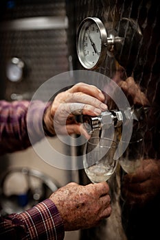 Old winemakers hands pouring a glass of wine from modern inox ta