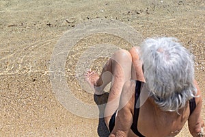 old woman in bathing costume sitting on sand next to the sea