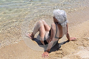 old woman in bathing costume sitting on sand next to the sea