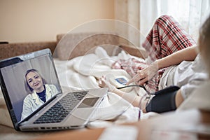 Old woman in bed looking at screen of laptop and consulting with a doctor online at home, telehealth photo