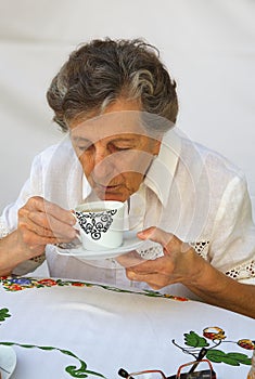 An old woman is blowing at hot tea while having her breakfast