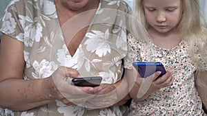 Old woman and child use smartphones at home. Modern grandmother and granddaughter with mobile gadgets