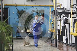 Old woman cleaner in workwear on manufacturing site