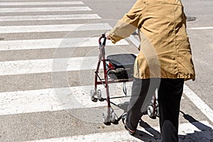 An old woman crosses a pedestrian crossing with the help of a rollator walker