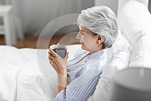 old woman with cup of coffee in bed at home