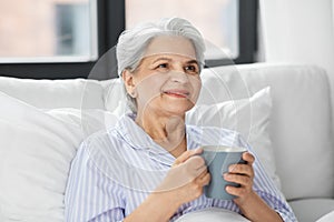 old woman with cup of coffee in bed at home