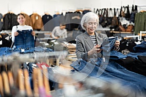 Old woman customer choosing jean pantaloons in clothing store