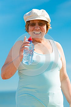 Old woman drinking mineral water in plastic bottle outdoor