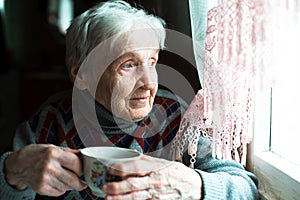 An old woman drinking tea sitting in the kitchen