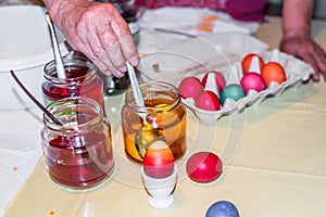 Old woman dyeing Easter eggs at home in the kitchen in the cucumber glass and with different colors, Germany