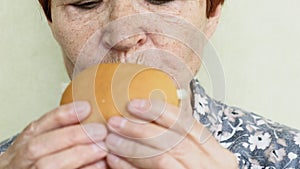 Old woman eating burger closeup, fast food