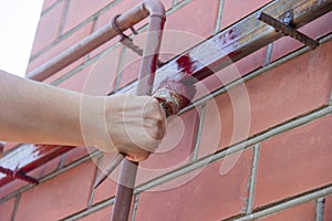 An old woman female hand paints a welded pipe construction canopy frame with a brush while standing on a stepladder