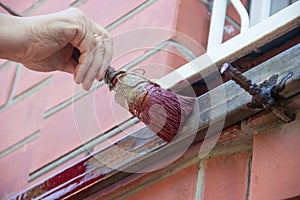 An old woman female hand paints a welded pipe construction canopy frame with a brush while standing on a stepladder