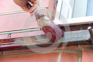 An old woman female hand paints a welded pipe construction canopy frame with a brush while standing on a stepladder