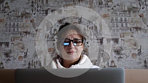 Old woman in glasses having a video call on the laptop smiling and talking happily indoors in a cozy apartment. doctor