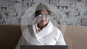 Old woman in glasses having a video call on the laptop smiling and talking happily indoors in a cozy apartment. doctor