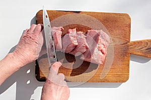 Old woman hand cutting pork meat on a chopping board. Top view. Cooking at home process