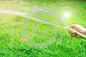 Old woman hand holding rubber water hose and using finger close end of rubber water hose to make water spray with sunlight