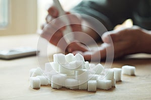 Old woman hands using lancet on finger to check blood sugar level, glucometer and sugar cubes on wooden table close up, diabetes photo