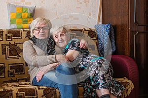 Old woman with her adult daughter cuddling on the couch. Family.