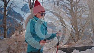 old woman hiking in the winter mountains. Senior female uses sticks for Nordic walking. Snowy peaks