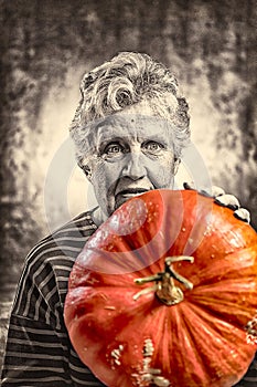 Old woman holding a big ripe pumpkin. Halloween theme.