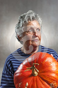 Old woman holding a big ripe pumpkin. Halloween theme.