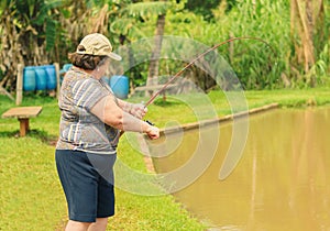 Old woman holding a fishing rod, hooking a fish on a lake.